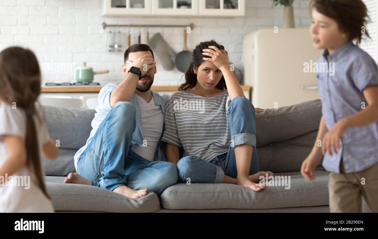 Tired young parents exhausted from loud kids playing Stock Photo