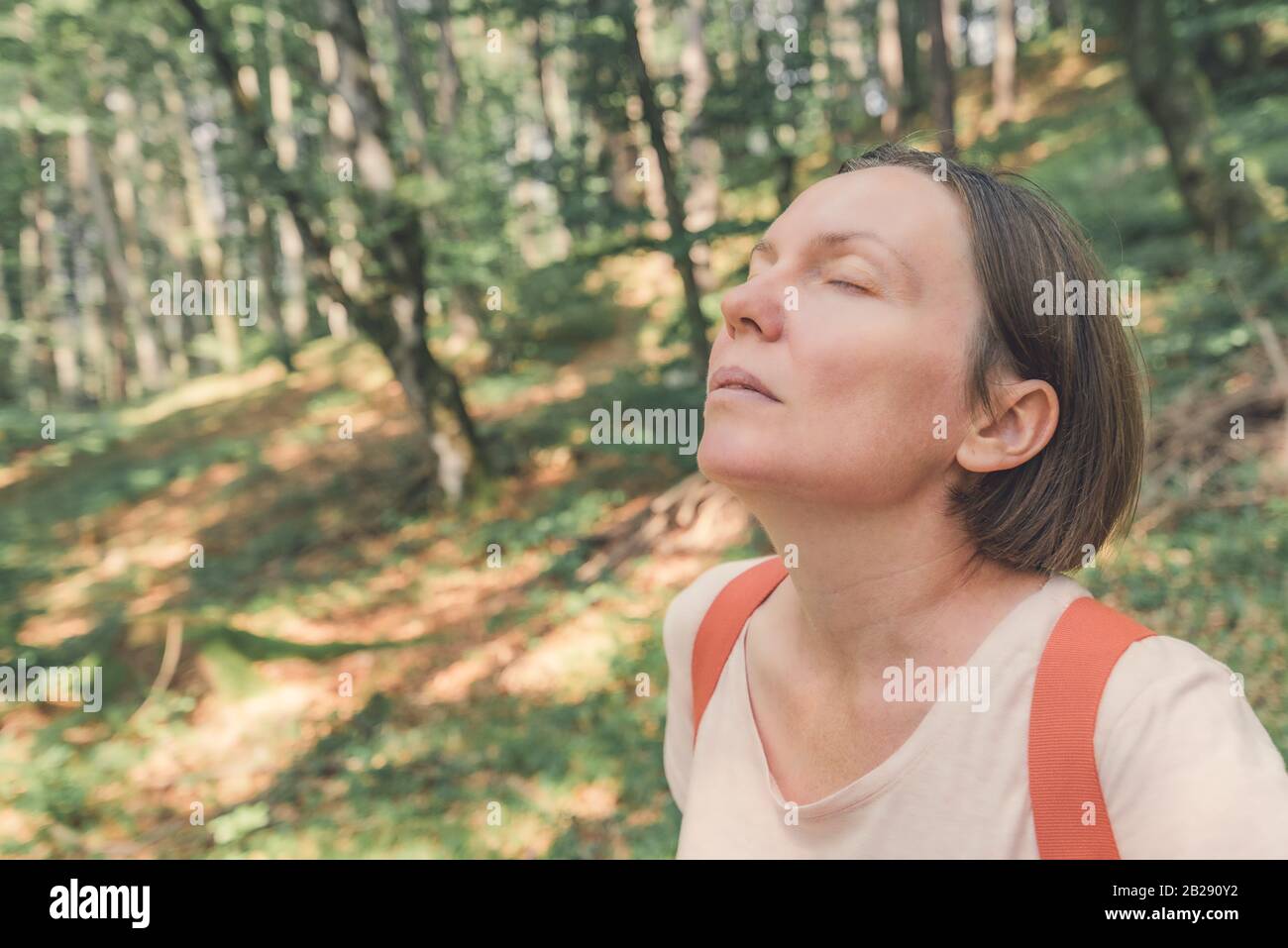 Female hiker taking breath of fresh air in forest and enjoying relaxing walk through woods Stock Photo