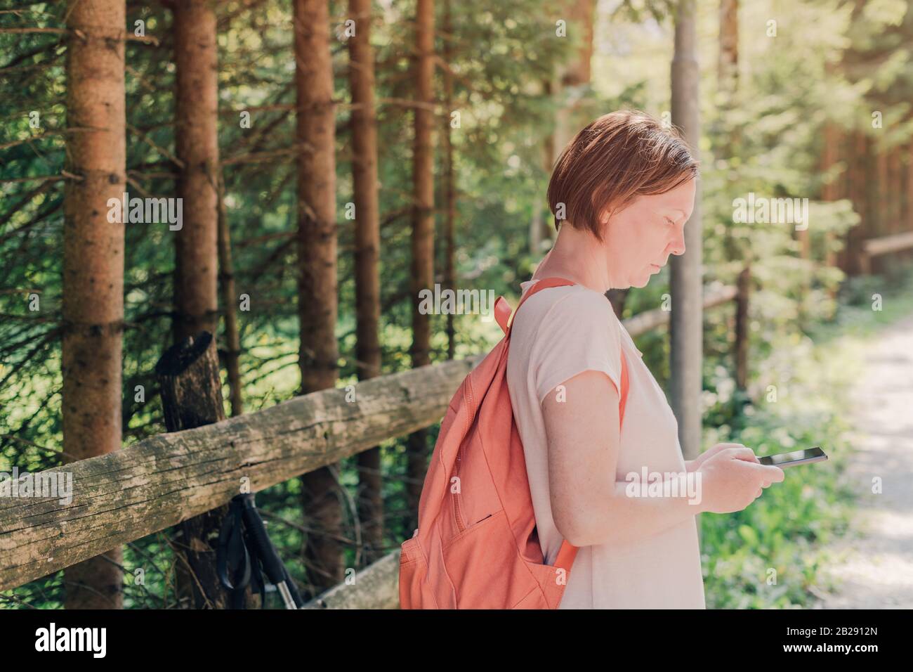 Female hiker text messaging on mobile phone by the road through countryside on sunny summer day during her vacation Stock Photo