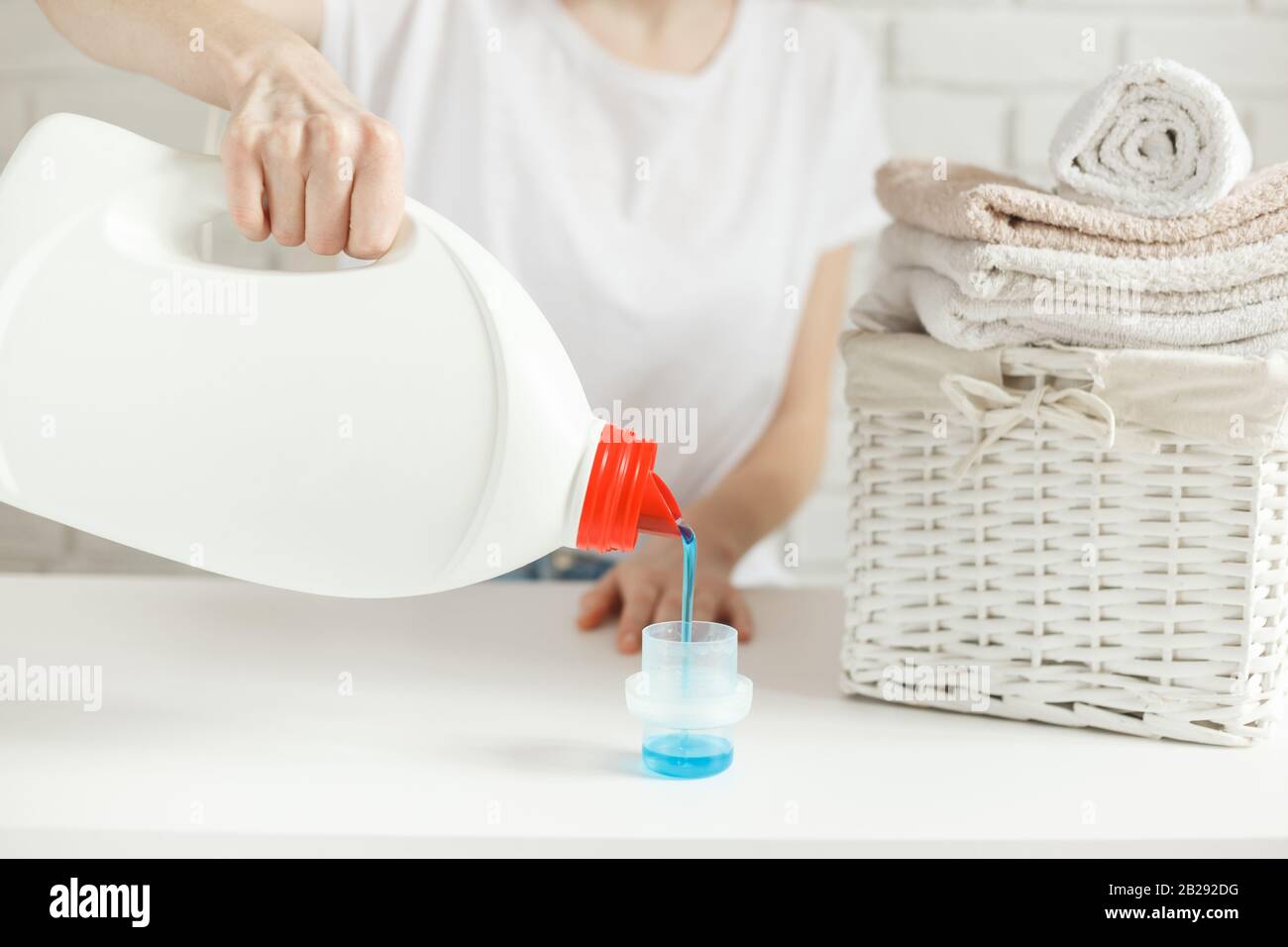 Woman pouring detergent into cap on table, closeup. Laundry concept
