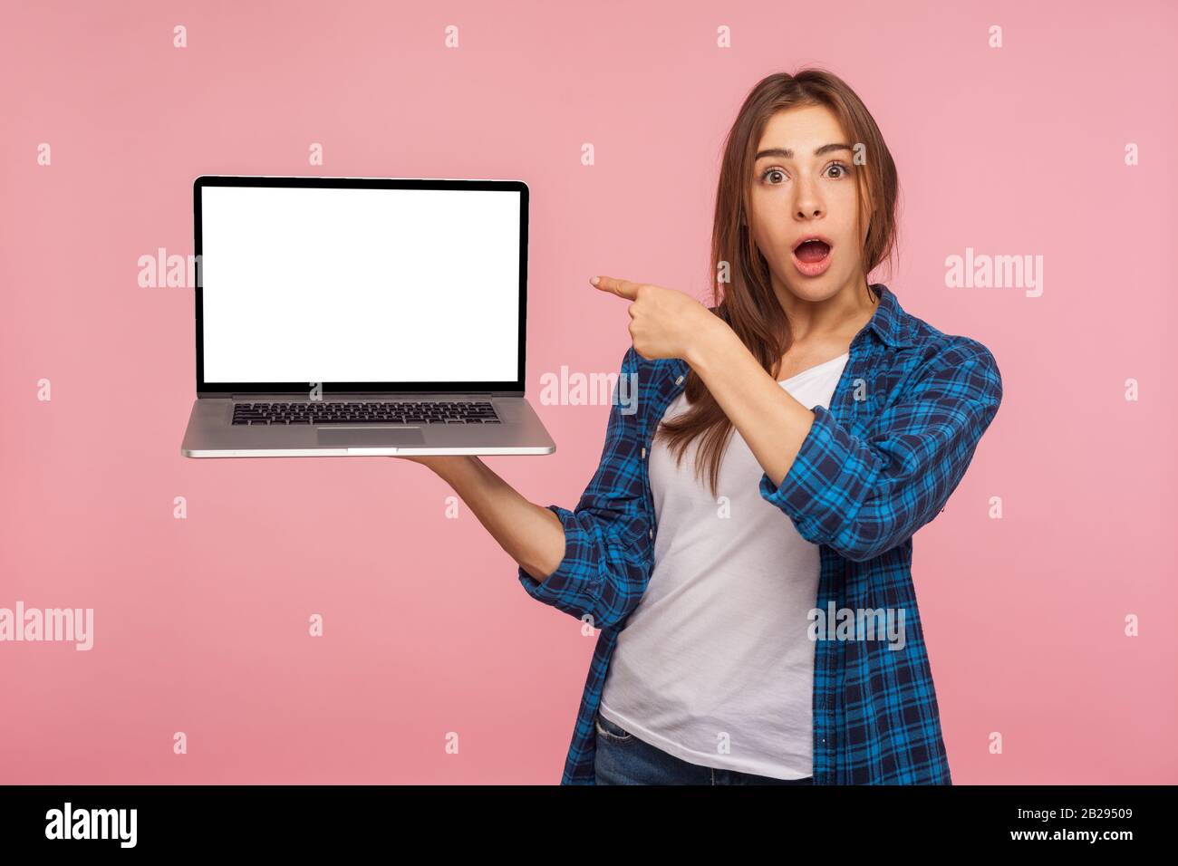 Portrait of amazed charming girl in checkered shirt showing blank laptop screen with shocked expression, pointing mock up, copy space for internet adv Stock Photo