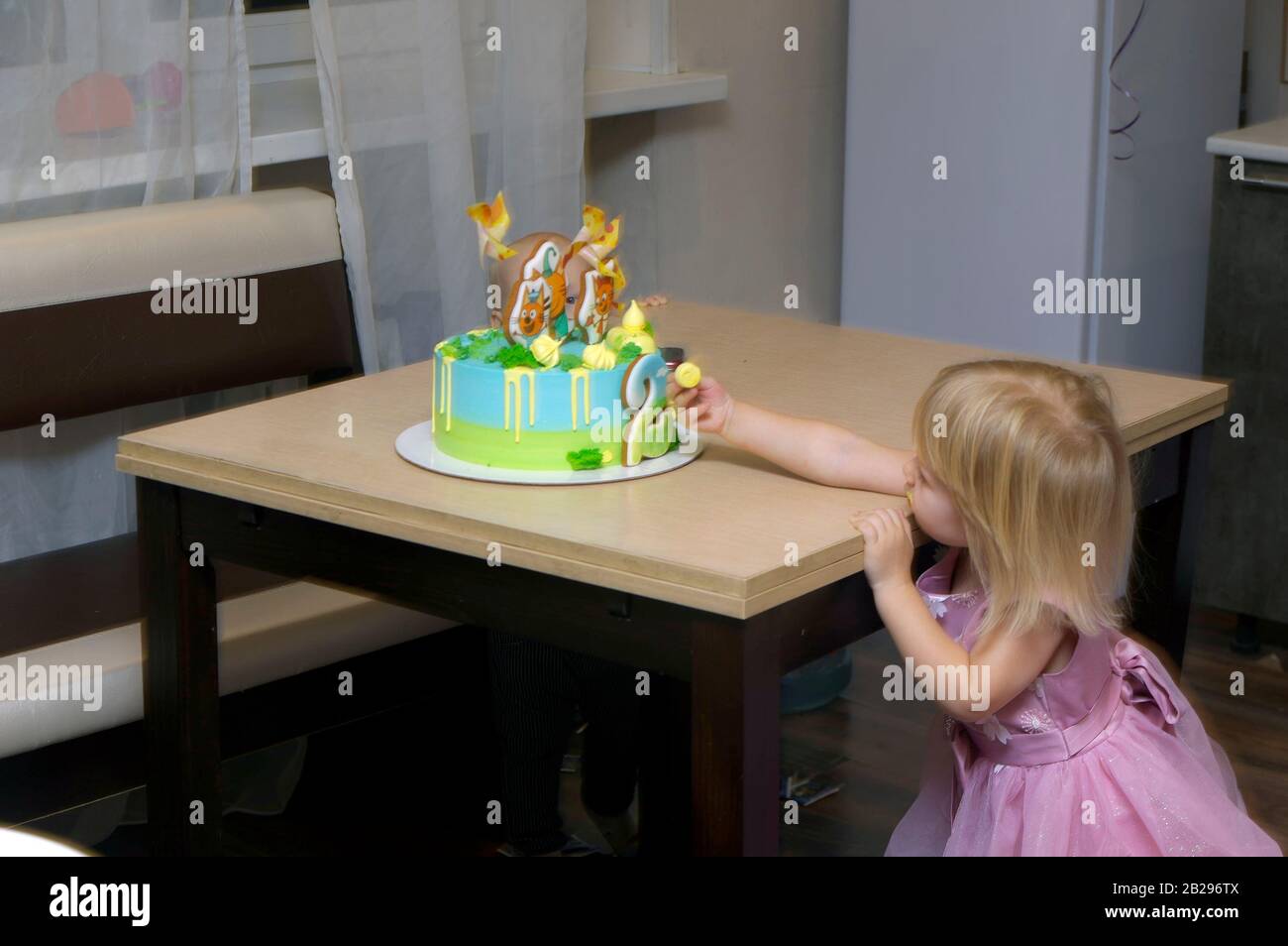girl pulls her hand to the cake standing on the table for her birthday Stock Photo