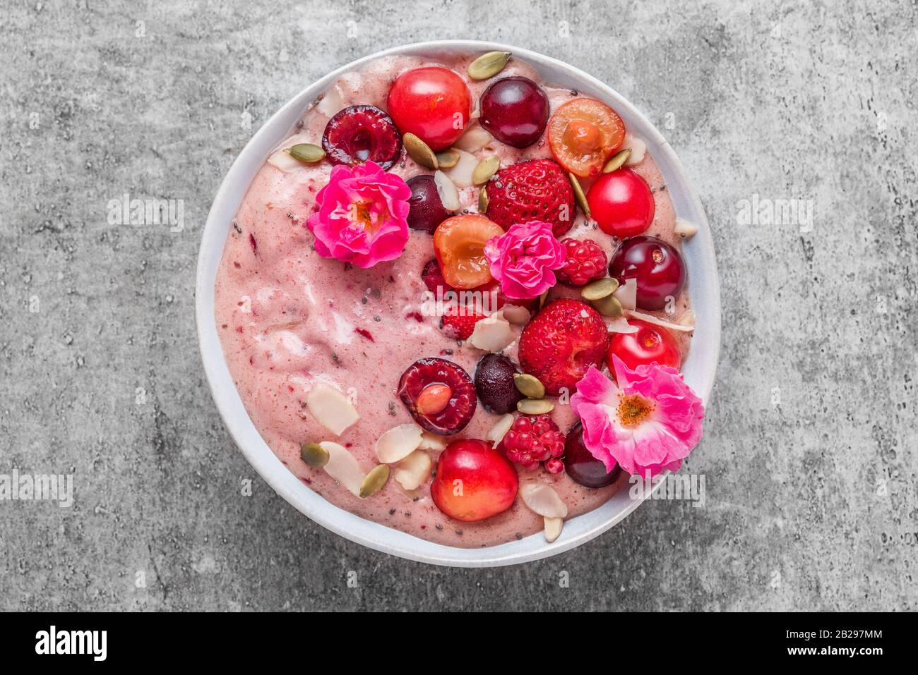 pink smoothie bowl or nice cream with fresh berries, rose flowers, nuts and chia seeds . healthy breakfast dessert. top view Stock Photo