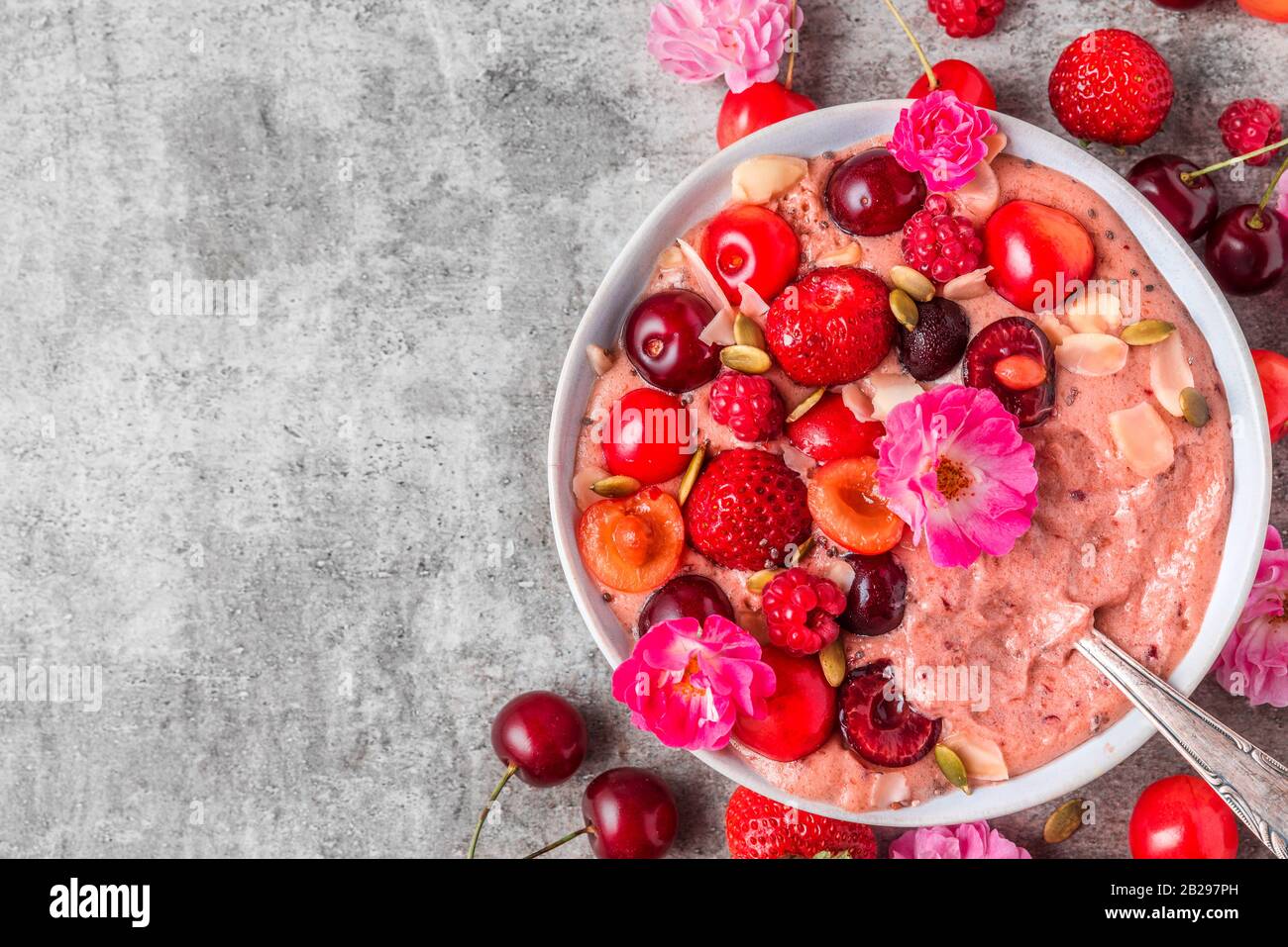 smoothie bowl or nice cream with fresh berries, rose flowers, nuts and chia seeds with a spoon . healthy breakfast dessert. top view with copy space Stock Photo