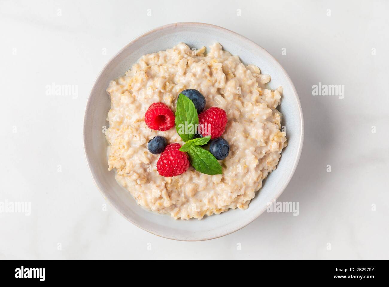 Oatmeal porridge in a bowl with fresh berries and mint on white background for healthy diet breakfast. top view Stock Photo