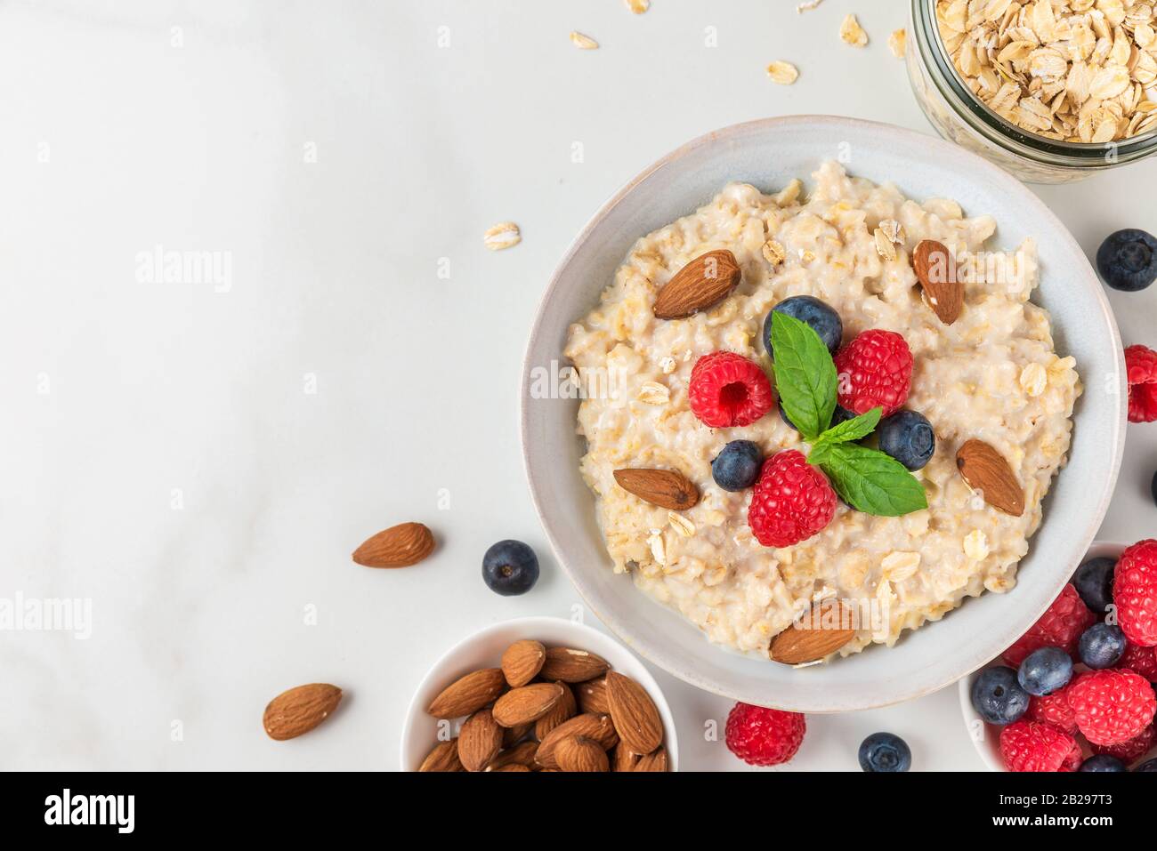 Oatmeal porridge in a bowl with fresh berries, almonds and mint on white background for healthy diet breakfast. top view with copy space Stock Photo