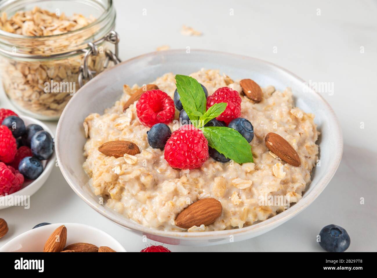Oatmeal porridge in a bowl with fresh berries, nuts and mint on white background for healthy diet breakfast. close up Stock Photo