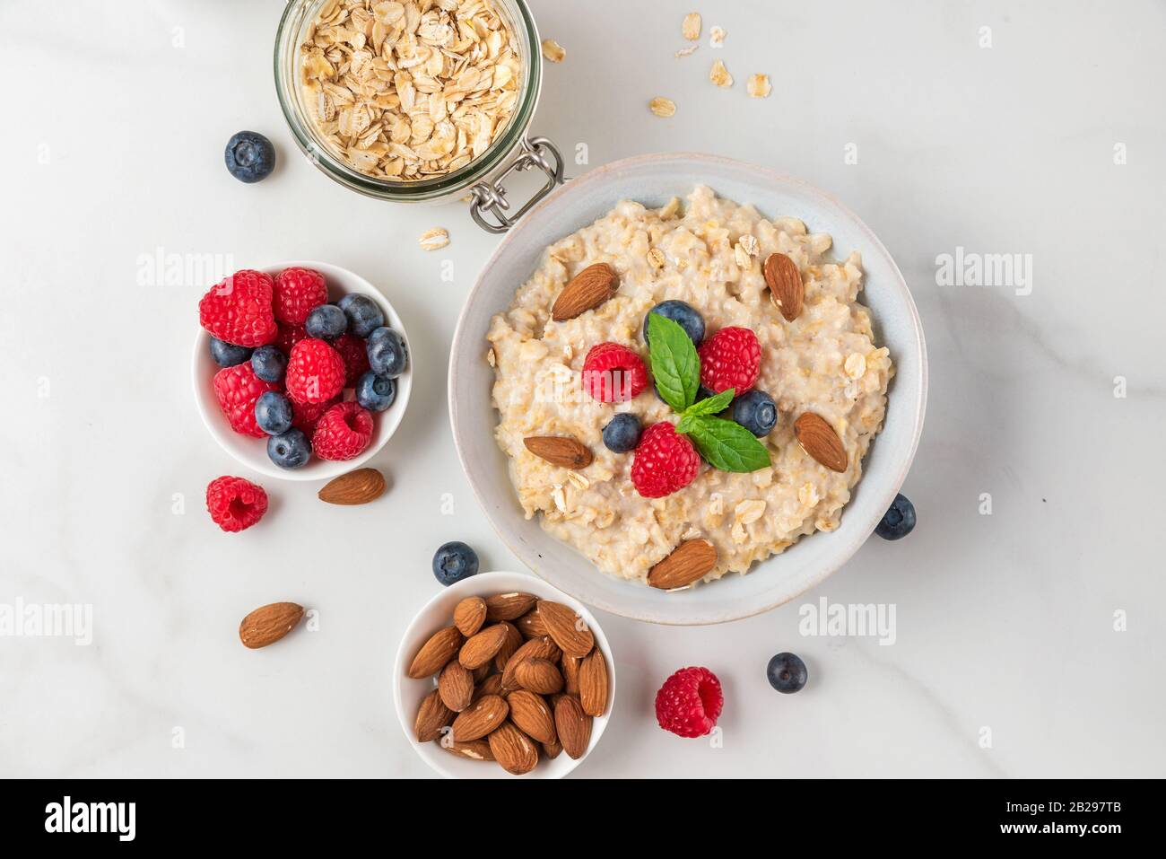 Oatmeal porridge in a bowl with fresh berries, nuts and mint on white background for healthy diet breakfast. top view Stock Photo