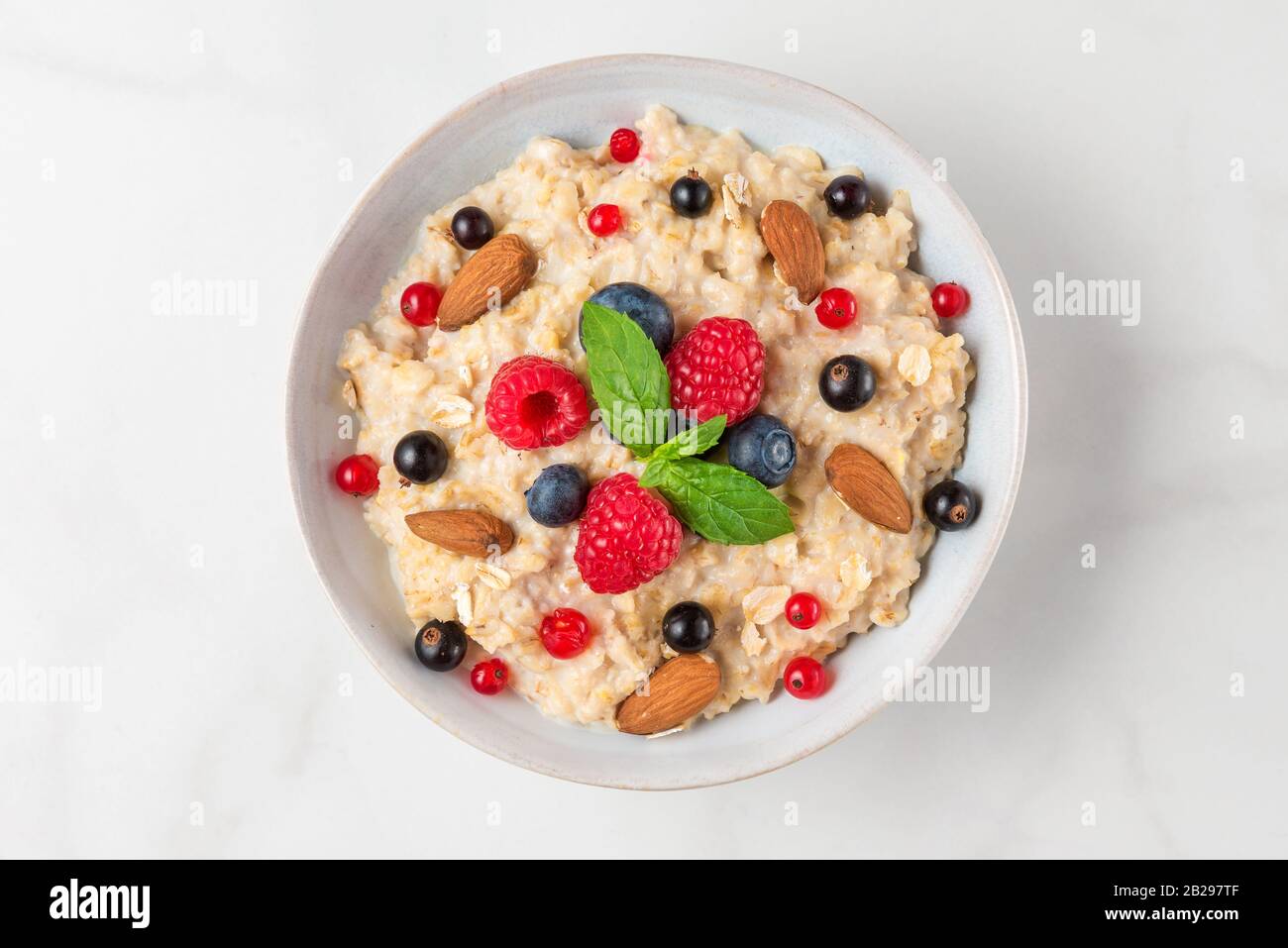 Bowl of oatmeal porridge with fresh berries, almonds and mint with for healthy diet breakfast on white table. top view Stock Photo