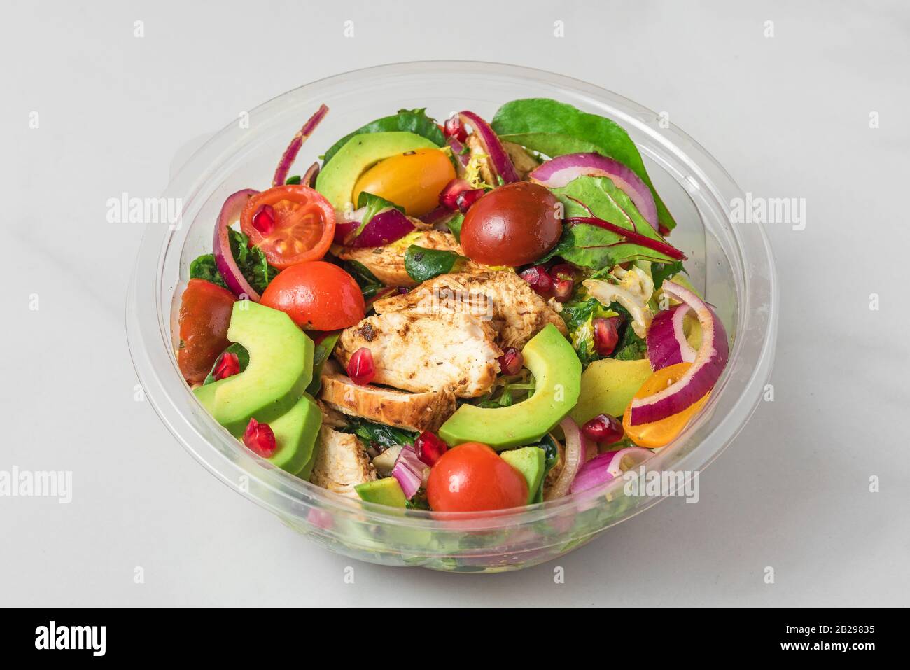 Healthy chicken salad with avocado, tomatoes and pomegranate in plastic package for take away or food delivery. close up Stock Photo