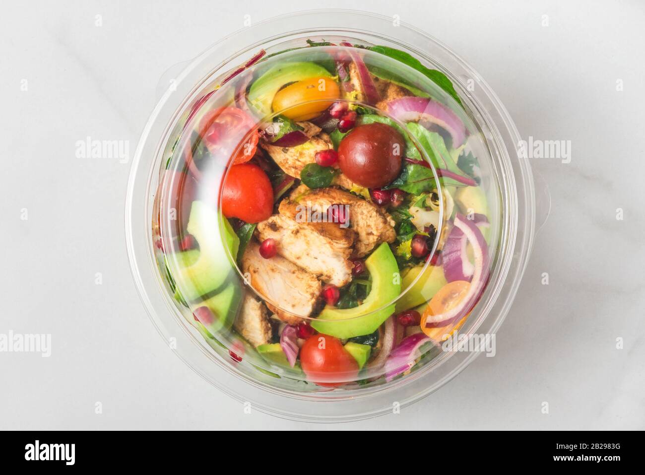 Plastic package with healthy chicken salad with avocado , tomatoes and pomegranate to take away. top view Stock Photo