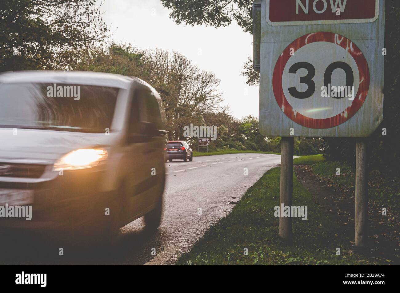 Speeding cards travel in opposite directions on a country line.  30 mph road sign on right of frame, with car driving past at speed. Stock Photo