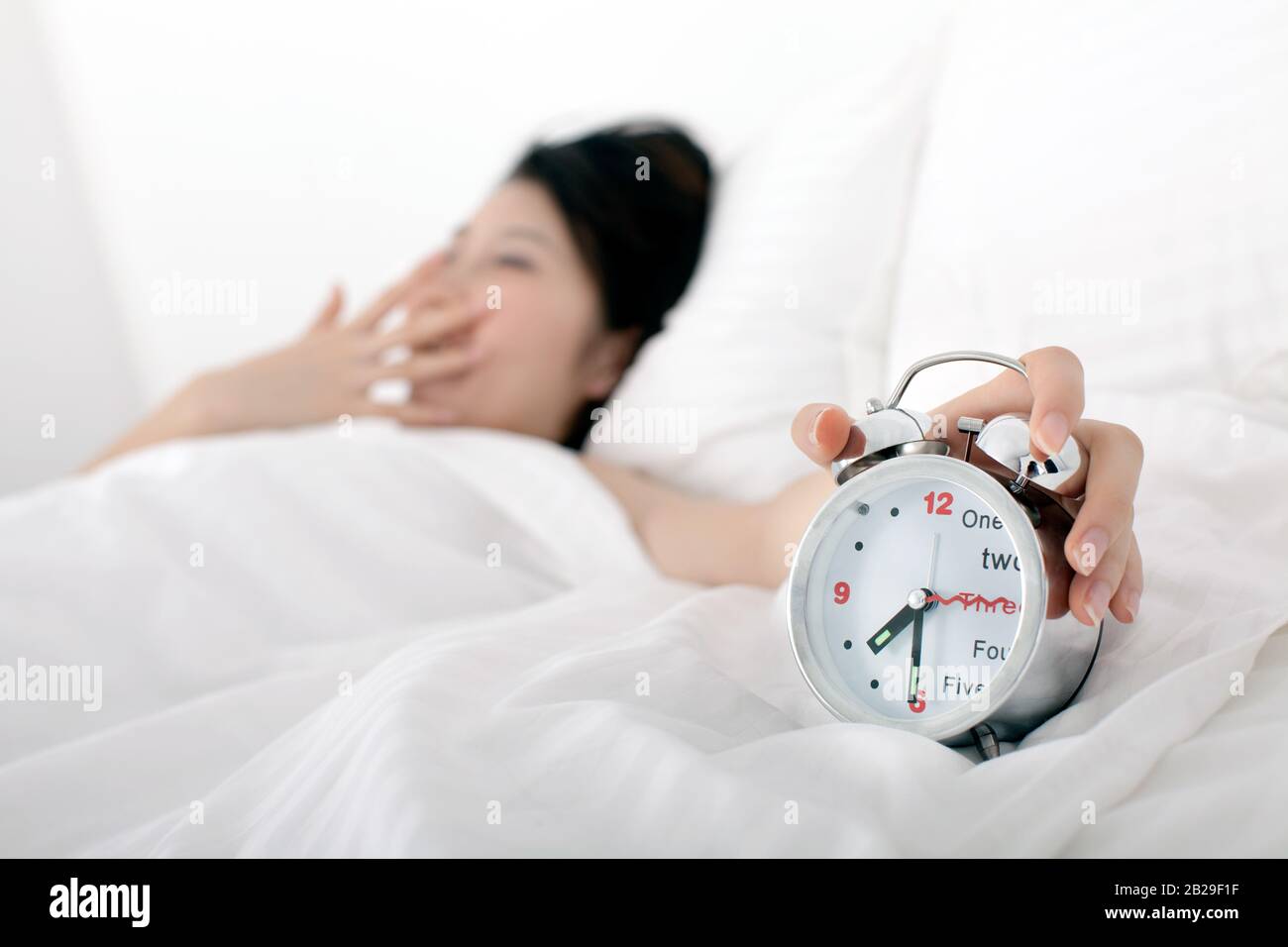 a woman is woken up by an alarm clock in the morning Stock Photo