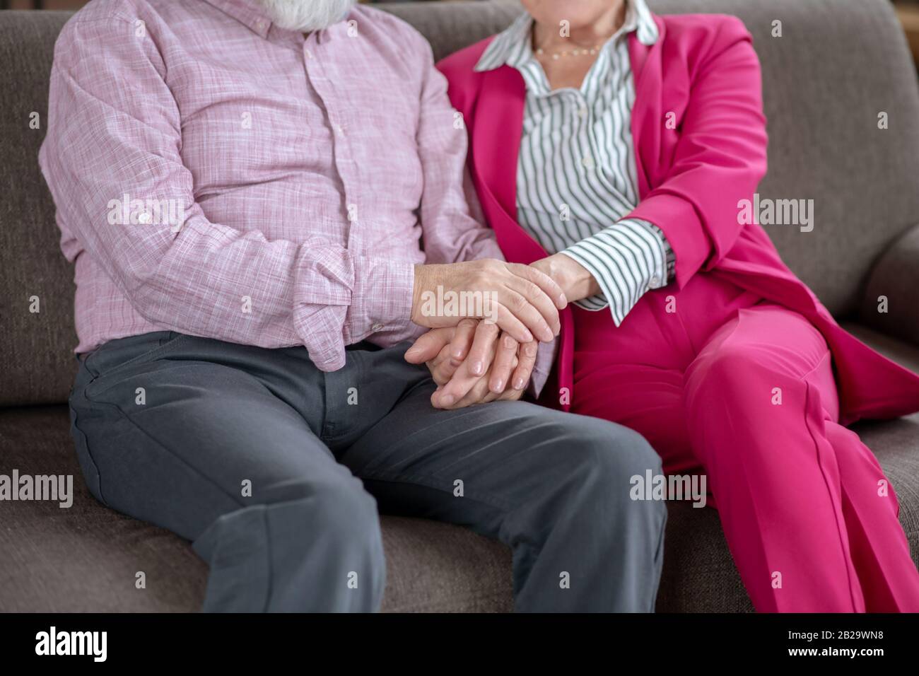 Husband and wife sitting on the sofa holding each others hands Stock Photo