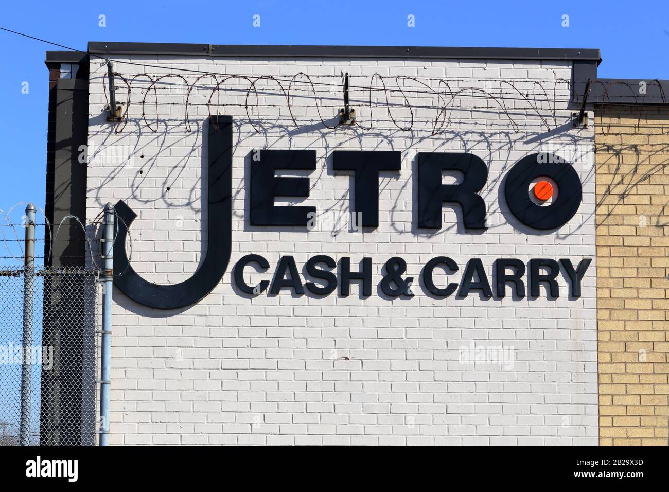 Jetro Cash & Carry logo on a brick wall adorned with barbed wire at one of their restaurant supply stores in New York, NY. Stock Photo