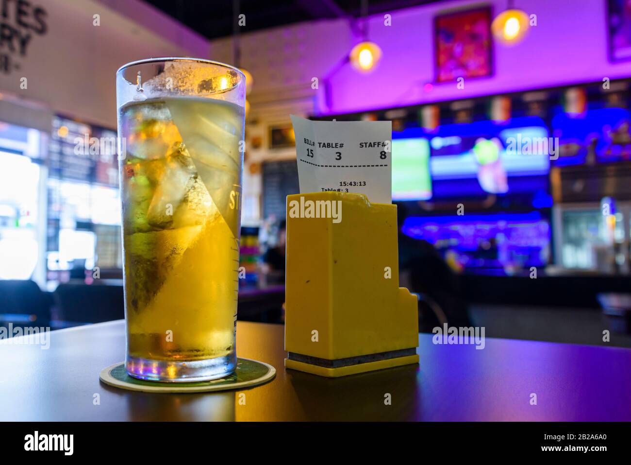 Pint of cider with ice, and the bill on a table at a sports bar Stock Photo