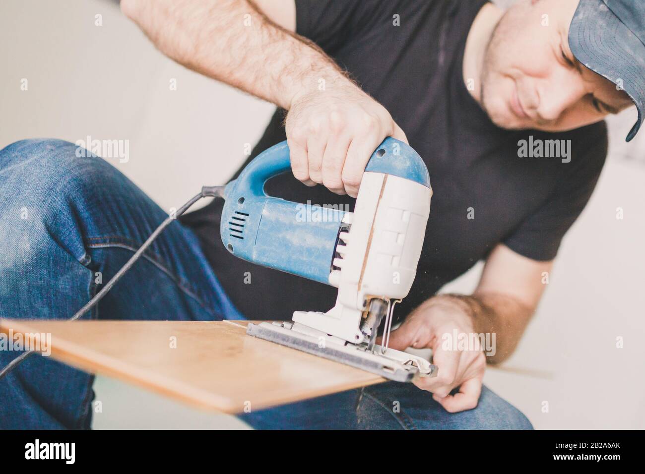 Adult male jigsaw cuts laminate by laying floating floor Stock Photo