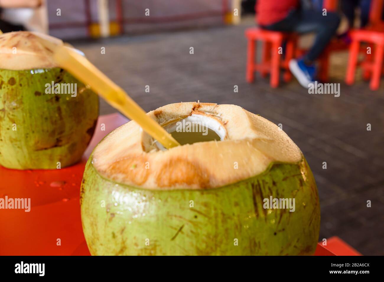 Coconut with a hole cut in the top and a plastic straw, very common drink in Thailand. Stock Photo