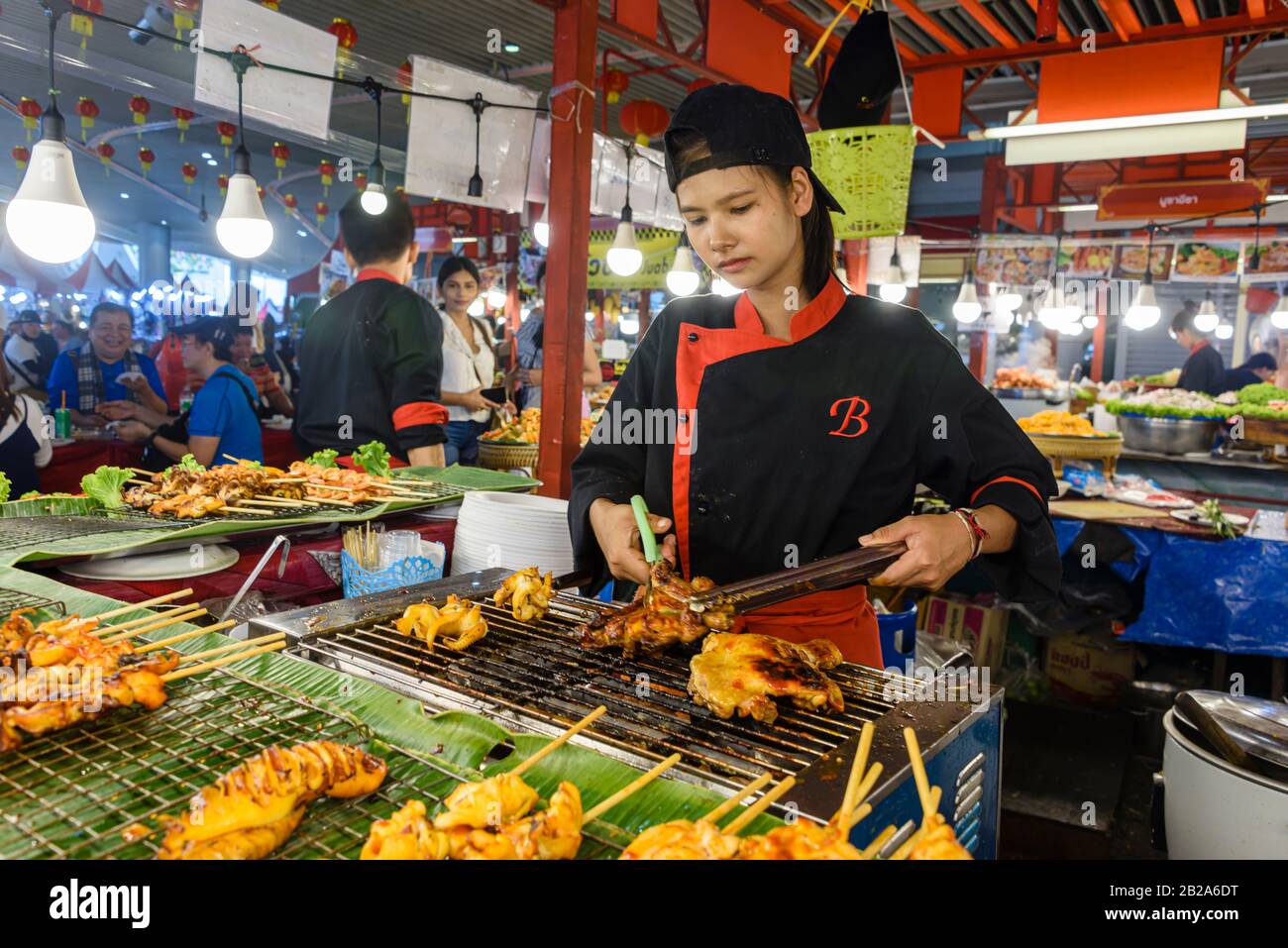 A young woman uses scissors to cut up grilled chicken at a street food stall, Bangkok, Thailand Stock Photo
