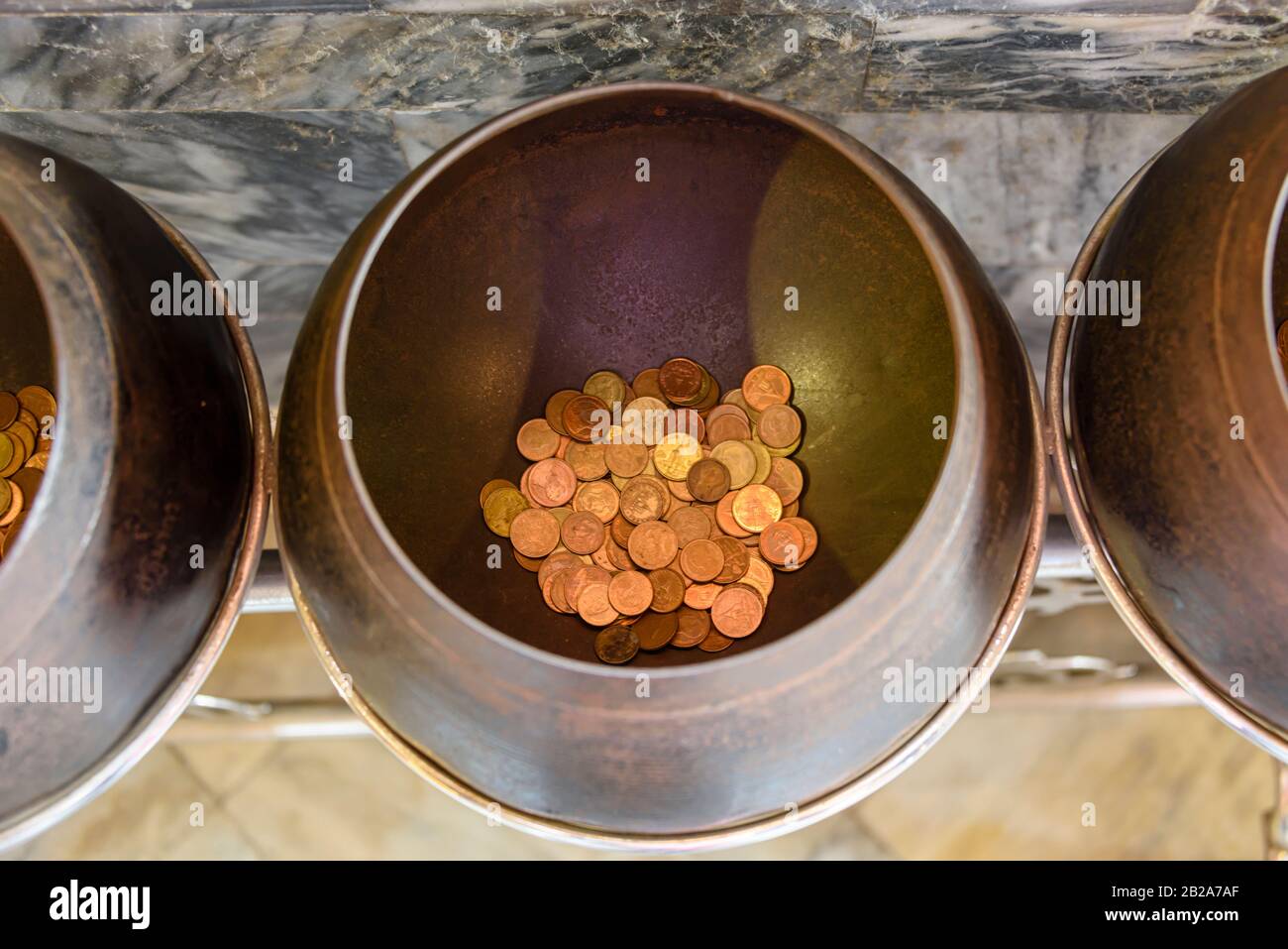 One of 108 old brass bowls with coins at Wat Pho.  It is believed placing coins in them brings good luck.  Bangkok, Thailand Stock Photo