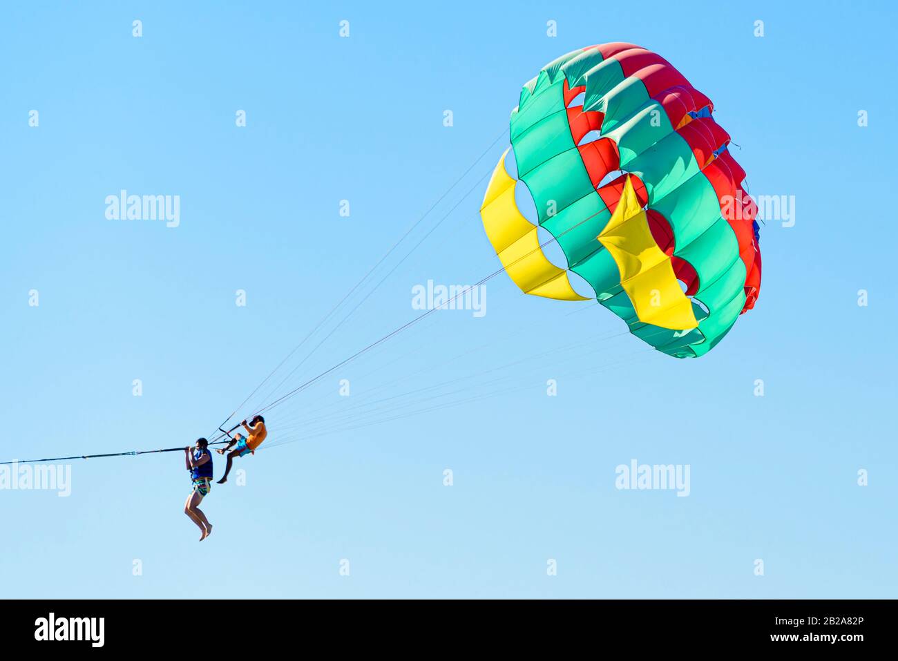 Tourist strapped into a parascending parachute while a Thai man sits on the ropes and holds on, Kata Beach, Phuket, Thailand Stock Photo