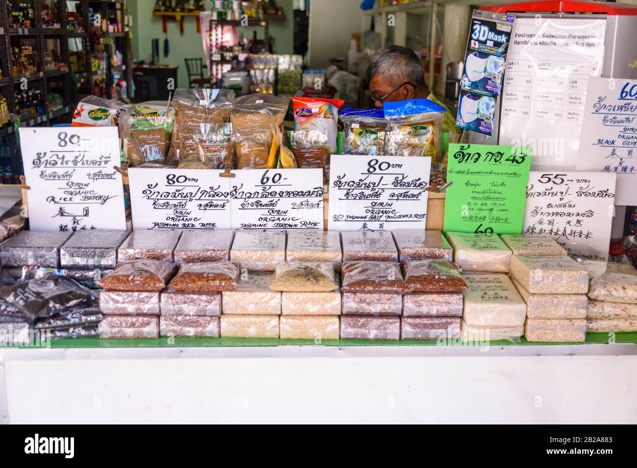 Packets of different varieties of rice outside a food shop with price signs in Thai and English, Thailand Stock Photo
