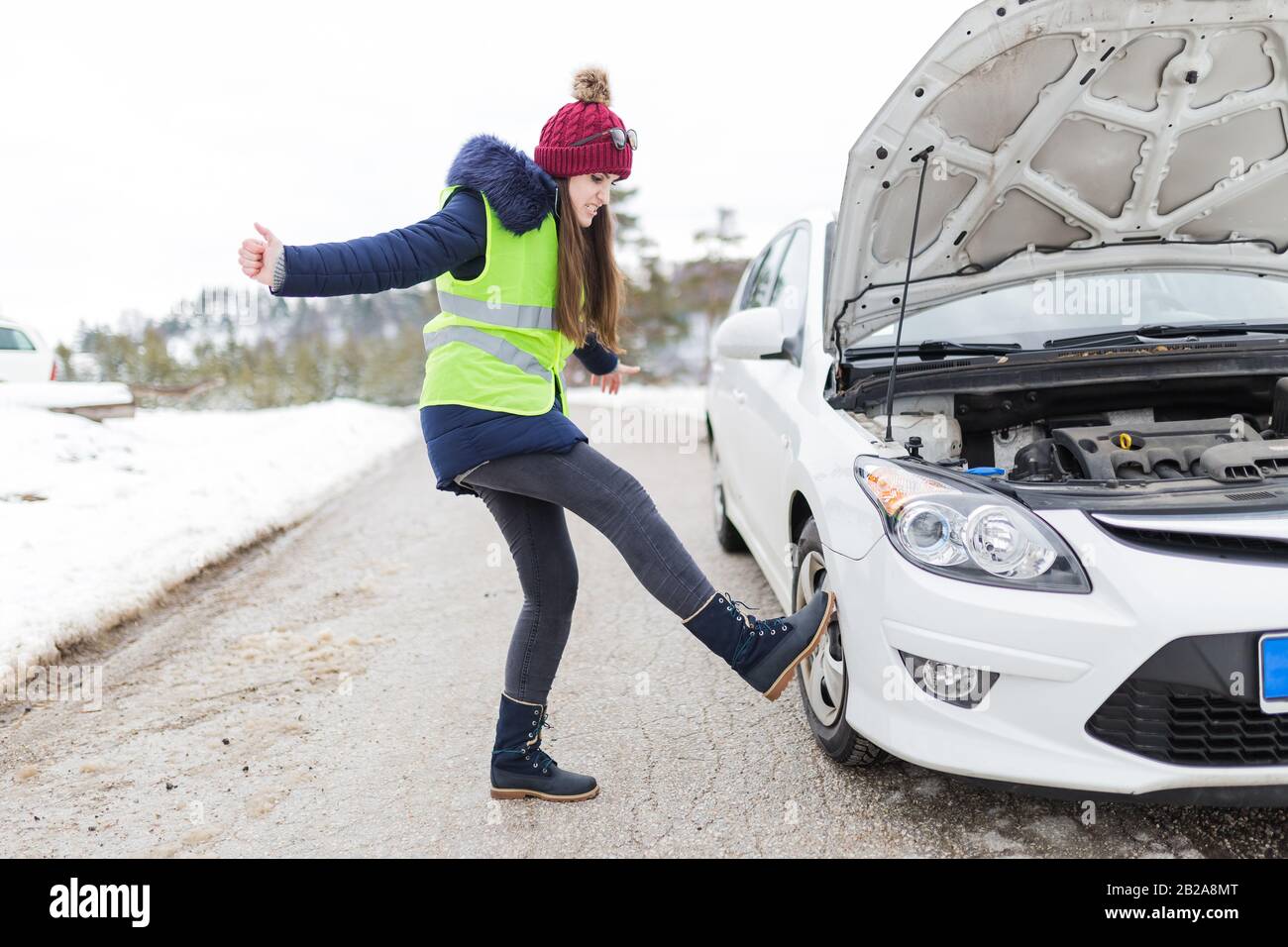 Angry woman kicking her broken car at roadside. Winter scene Stock