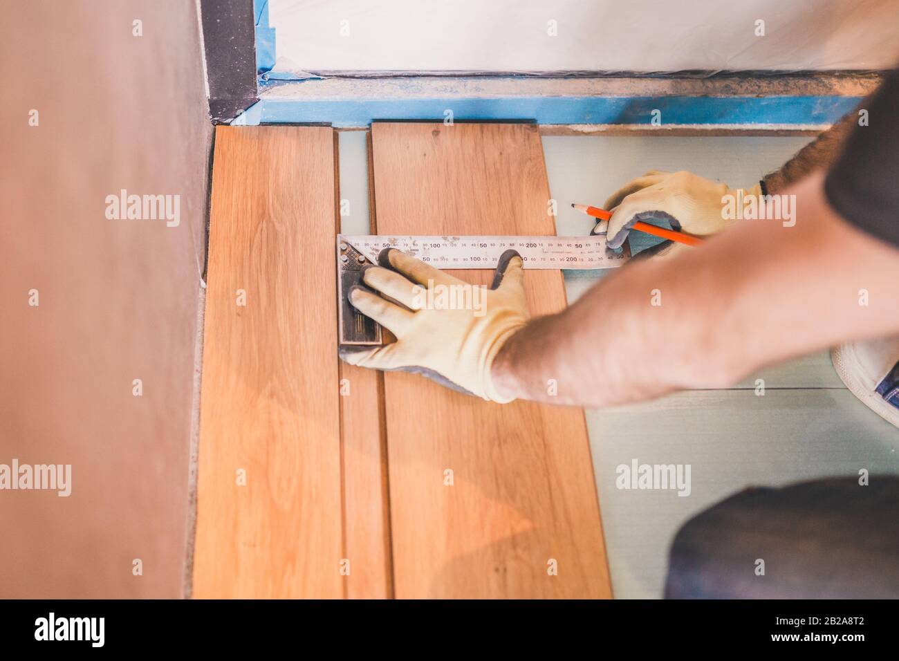 Worker measuring and marking laminate for cutting - installing floating floor - close-up on hands - home renovation concept Stock Photo