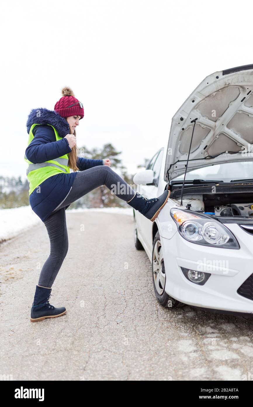 Mad woman kicking car with opened hood. Road assistance concept Stock