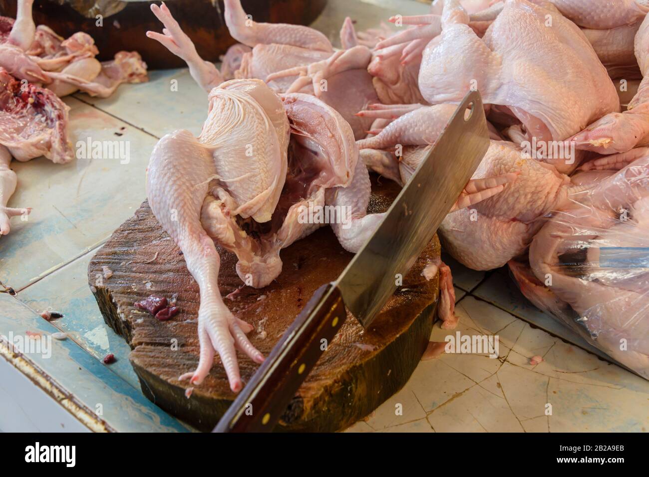 Large cleaver on a wooden chopping board with a number of chicken carcasses at a Thai butchers, Thailand Stock Photo