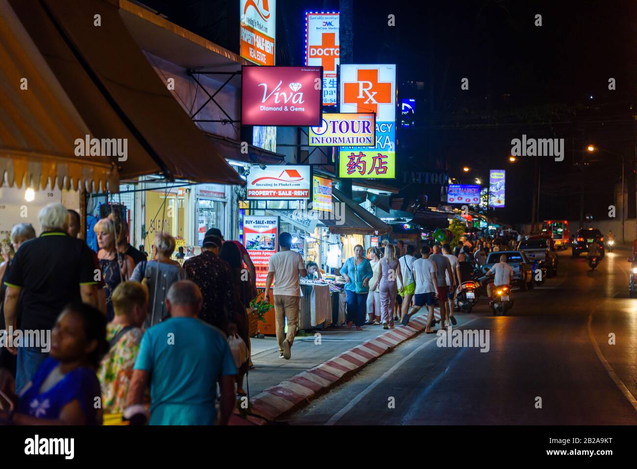 Tourists walk along the footpath outside shops at night, Kata Beach, Phuket, Thailand Stock Photo