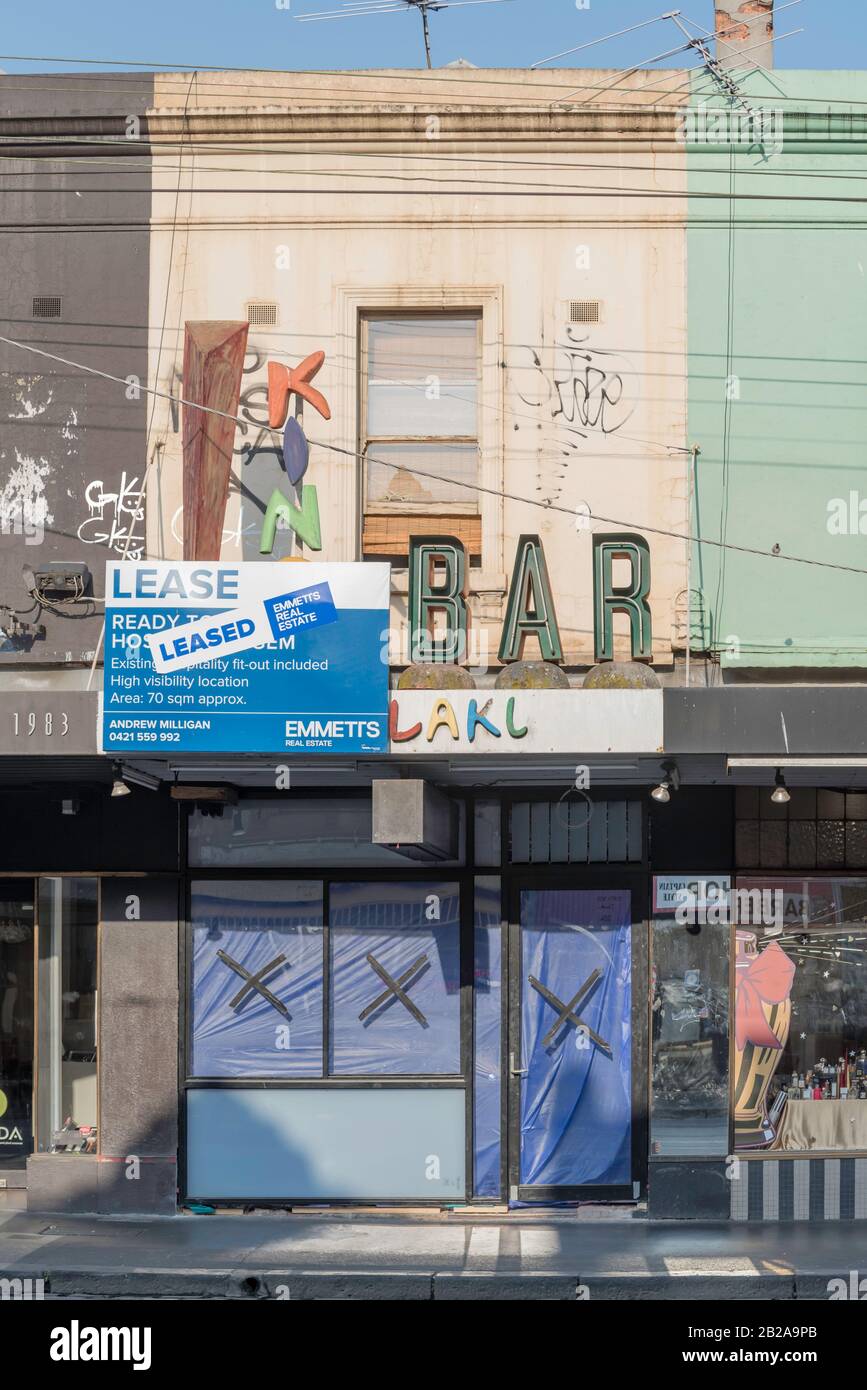 A For Lease sign and a large Leased decal sticker and below it a shop or store with its windows and front door covered in plastic hiding the interior Stock Photo