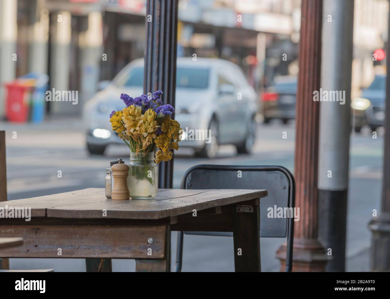 A colourful small bouquet of flowers sit in a jar on a rustic wooden table outside a cafe on busy Brunswick Street in Melbourne, Australia Stock Photo