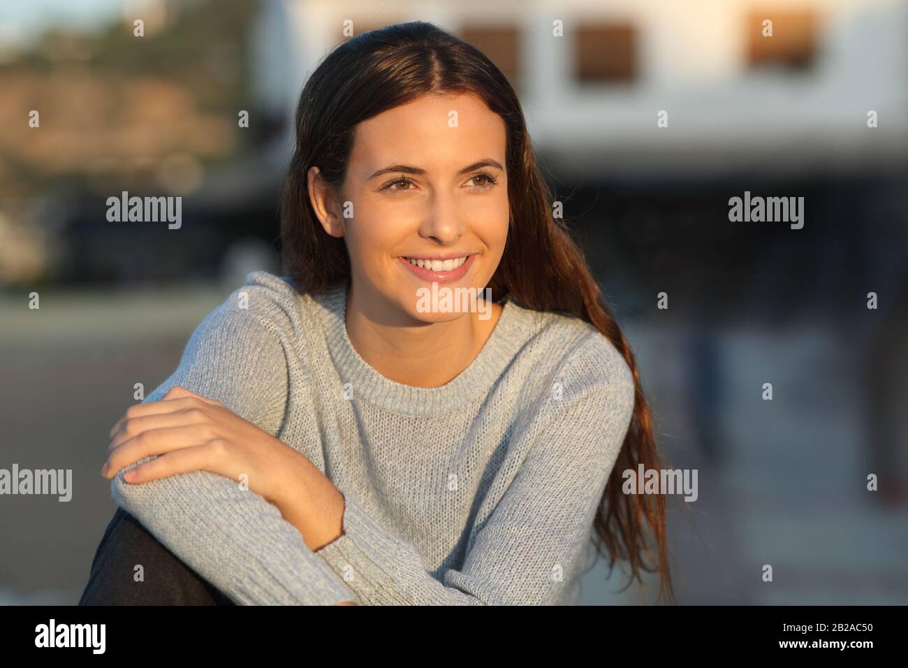 Portrait of a happy teenage girl smiling looking away at sunset in a town Stock Photo