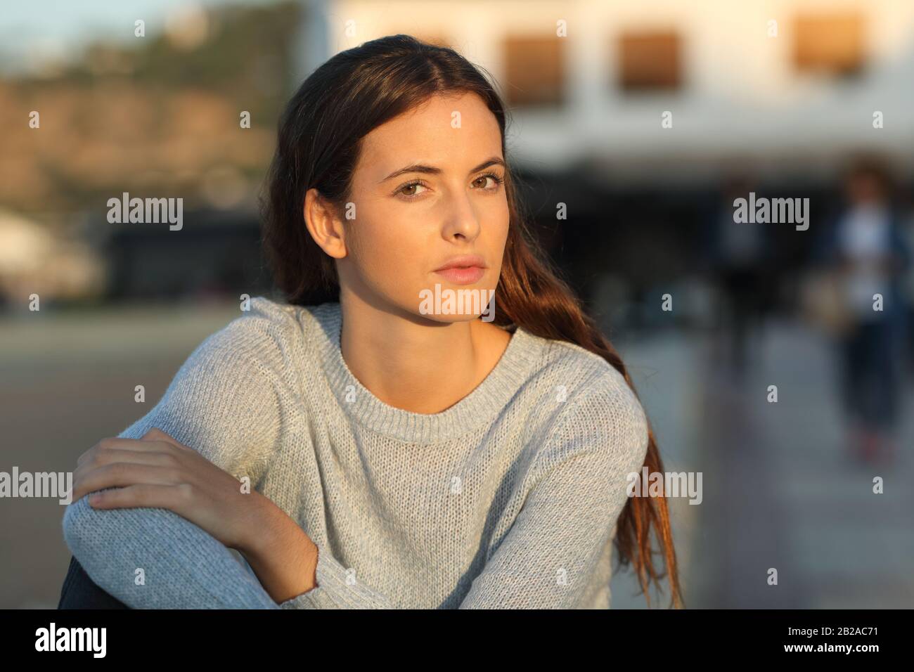 Serious teenage girl looking at camera defiant at sunset sitting in a town Stock Photo