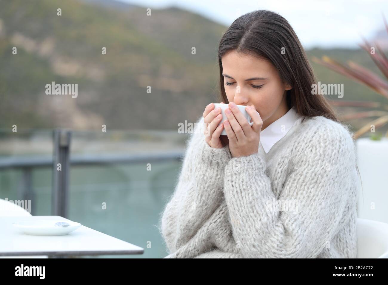 Girl smelling her coffee sitting in a cafe terrace in a lake in the mountain Stock Photo