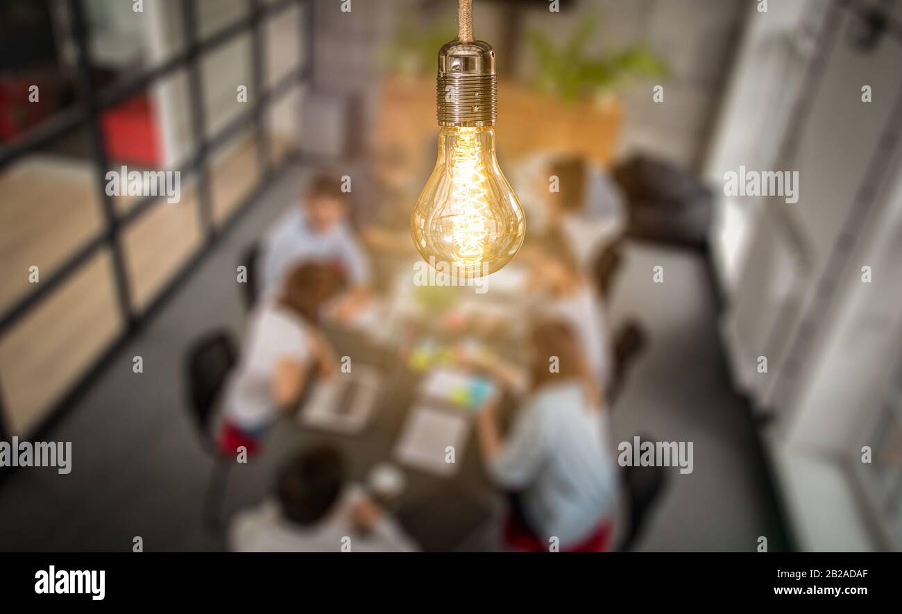 Young business people are discussing together a new startup project. A glowing light bulb as a new idea. Stock Photo