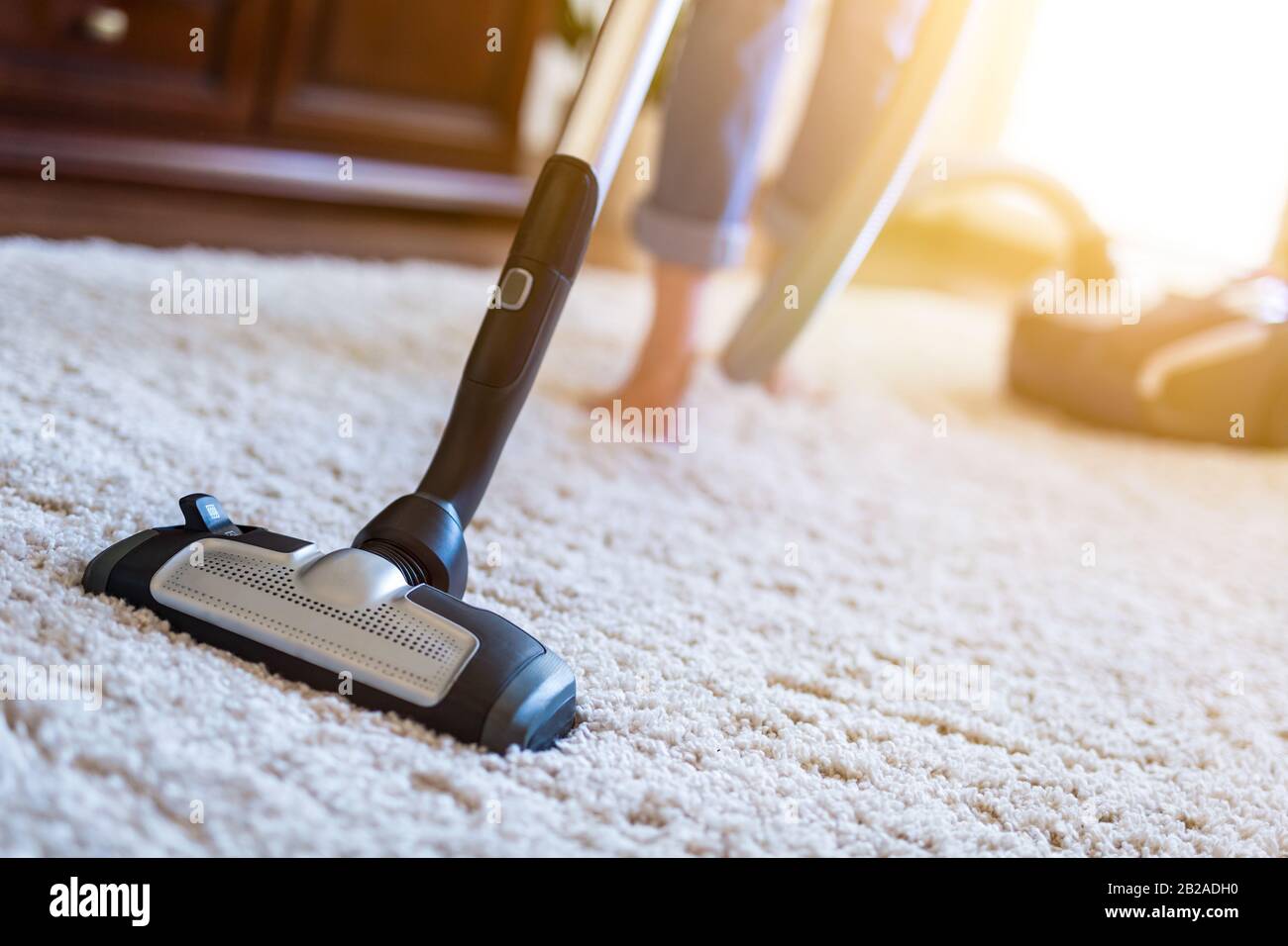 Young woman using a vacuum cleaner while cleaning carpet in the house. Stock Photo