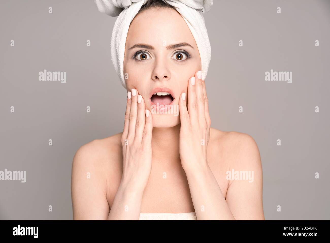 Shock and surprised - portrait of a beautiful young woman. Open mouth with surprise. Copy space on a gray background. Topics of beauty and spa. Stock Photo