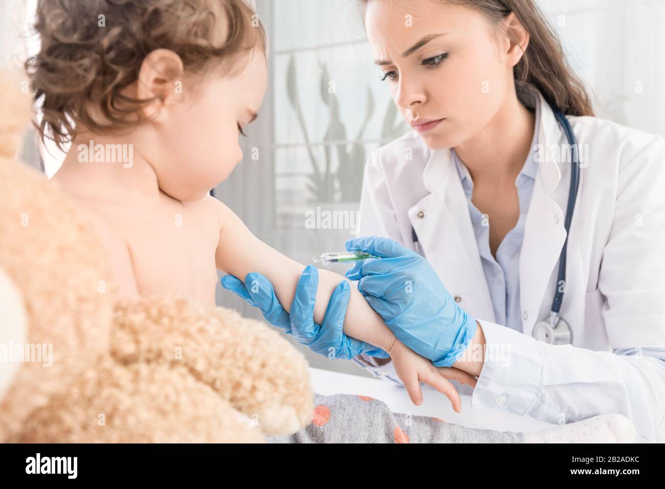 Young woman pediatrician performs a vaccination of a little girl. The girl is holding a mascot. Stock Photo