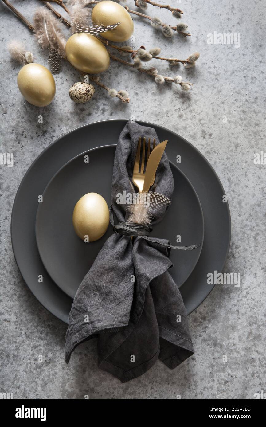 Easter table setting with black and golden decor on grey stone table. Top view. Vertical format. Stock Photo