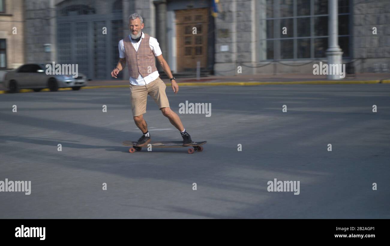 European mid-aged man keeps balance and rushing on a longboard Quickly through sity street. Stock Photo