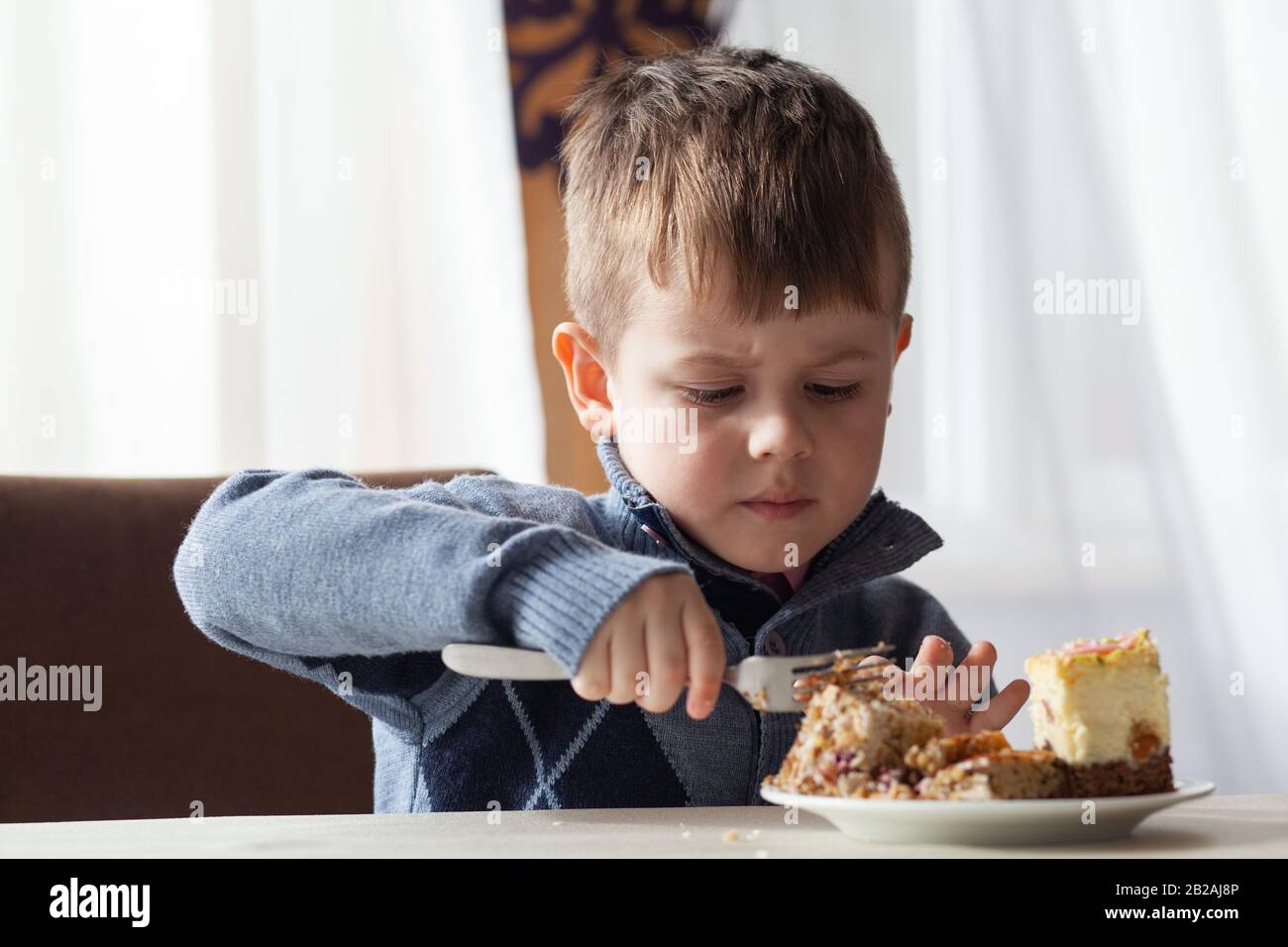 Cute little boy in cafe eat a big piece of cake with a fork. Desserts