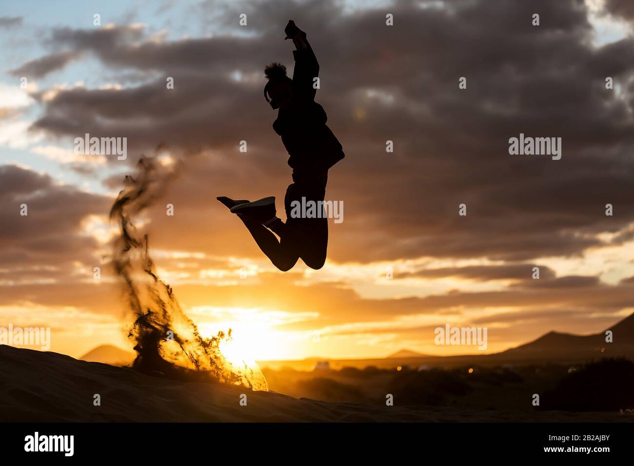 Silhouette of anonymous person leaping up on sandy coast against beautiful cloudy sundown sky. Stock Photo
