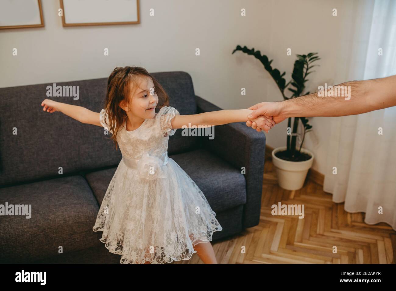 Caucasian father dancing with his small dressed in white daughter while having joy in the living room Stock Photo