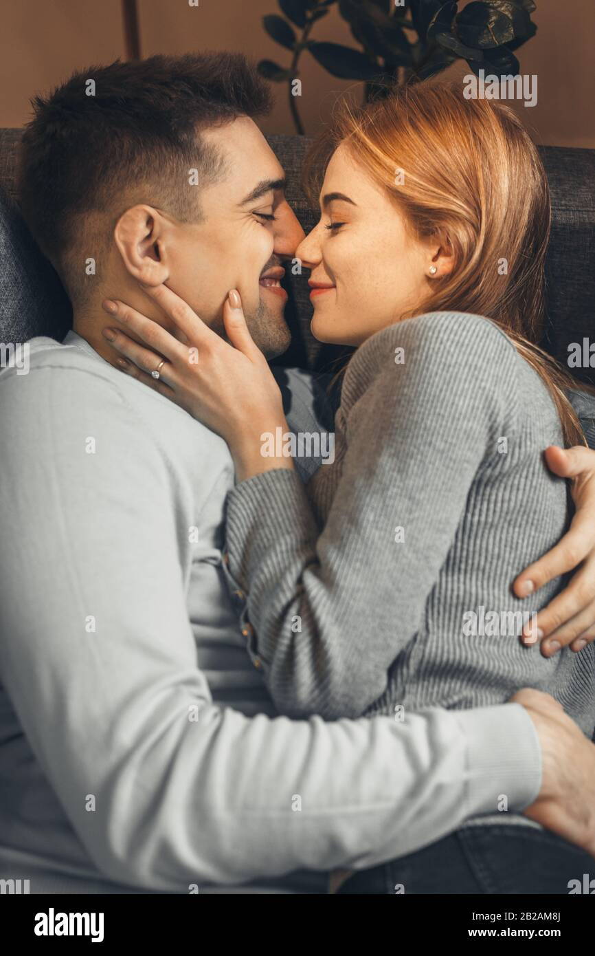 Handsome caucasian boy holding his girlfriend with red hair and freckles while lying on the sofa Stock Photo