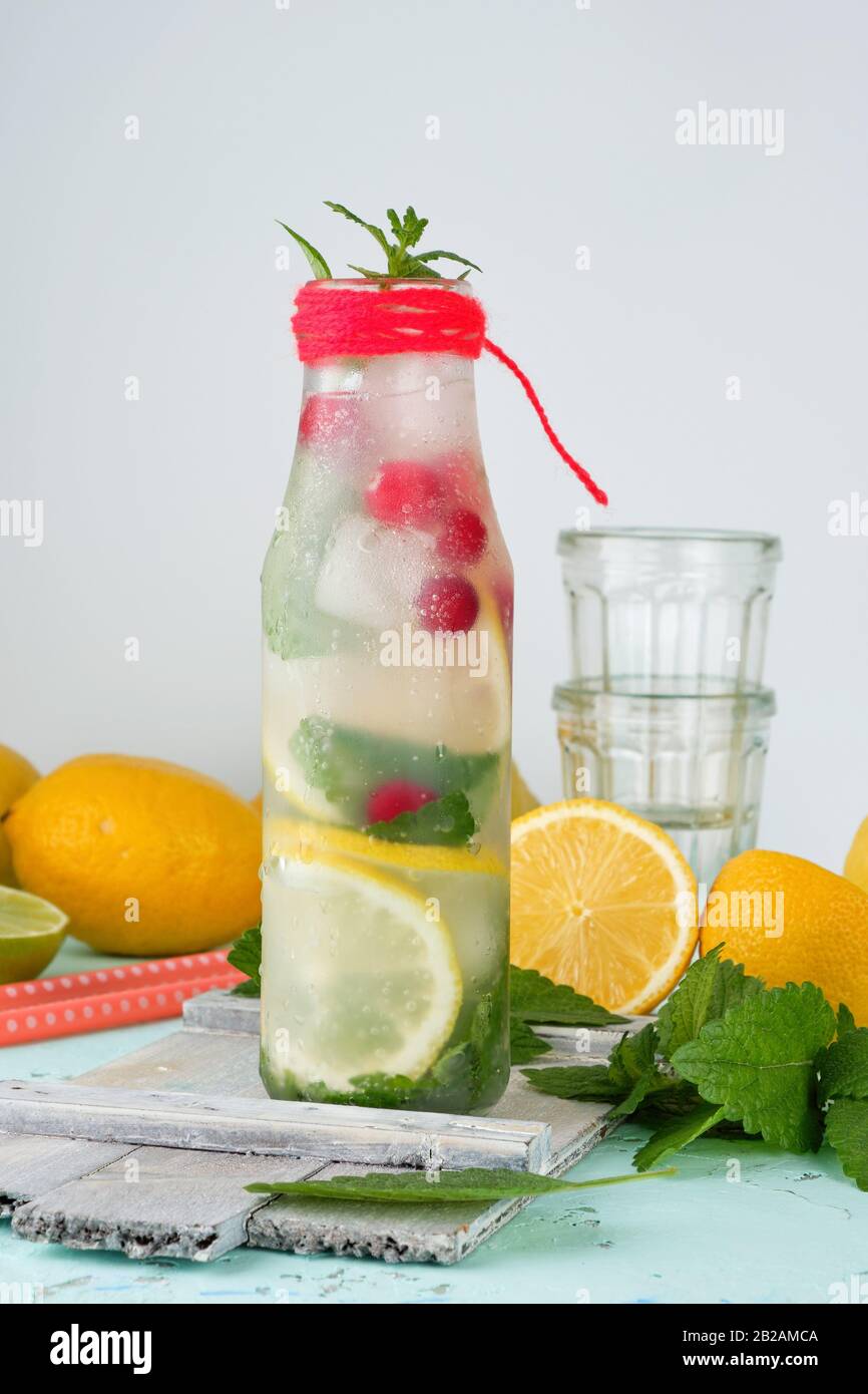 summer refreshing drink lemonade with lemons, cranberry, mint leaves, lime in a glass bottle, next to the ingredients for making a cocktail. Stock Photo