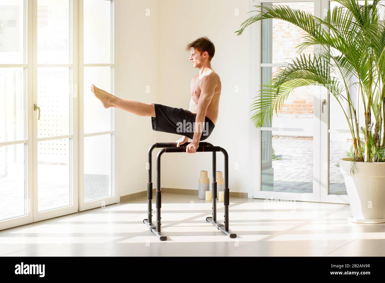 Fit young man working out on parallel bars doing V sit exercises during a calisthenics workout in a modern high key gym in a health and fitness concep Stock Photo
