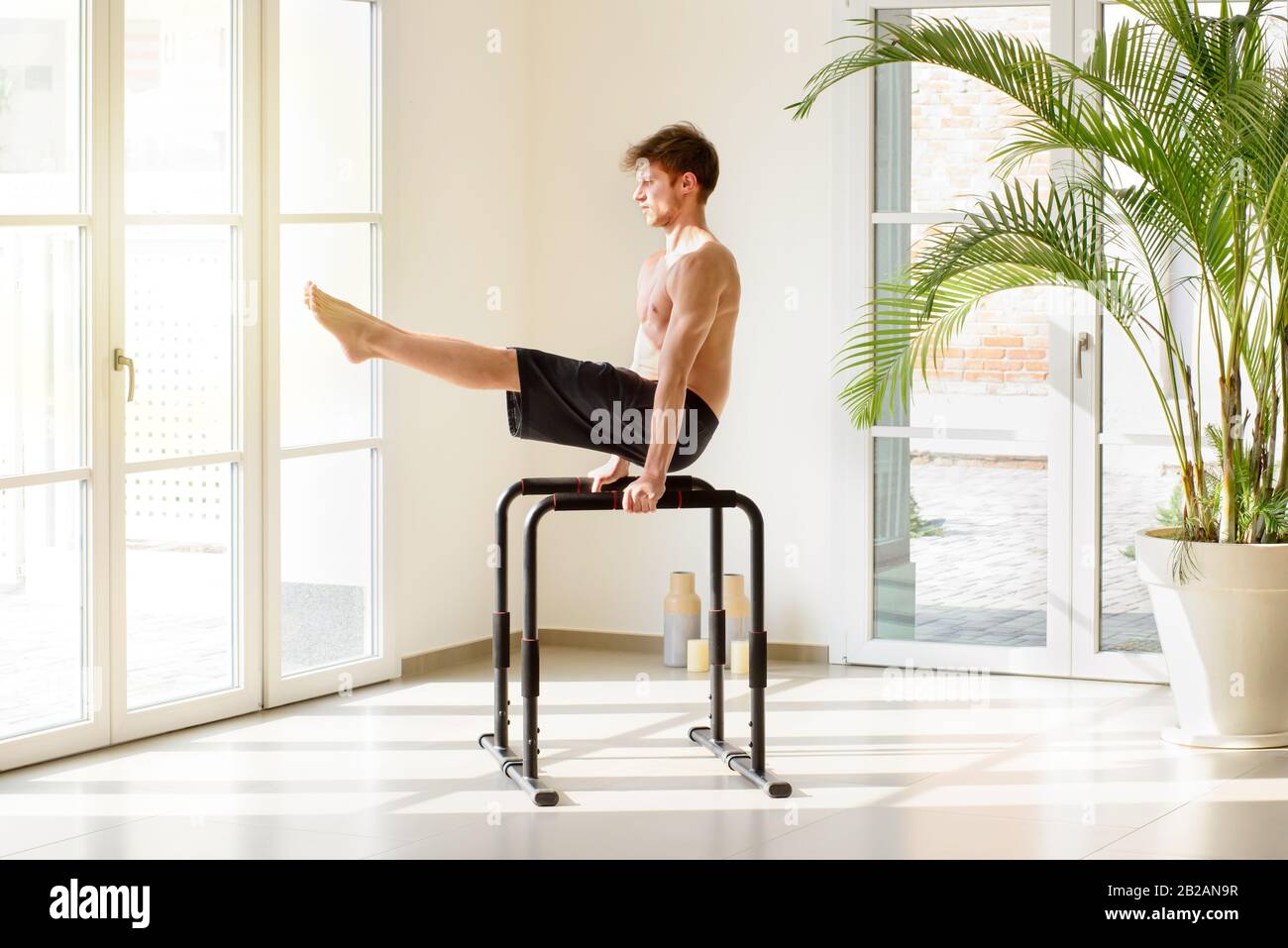 Fit young man working out on parallel bars doing V sit exercises