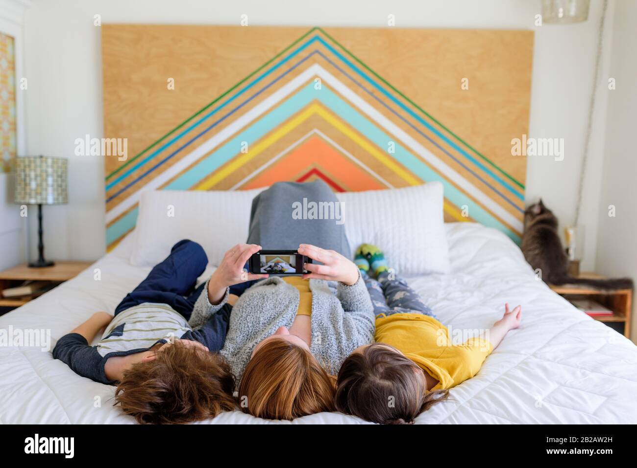 Mother lying on bed with two children taking a selfie Stock Photo
